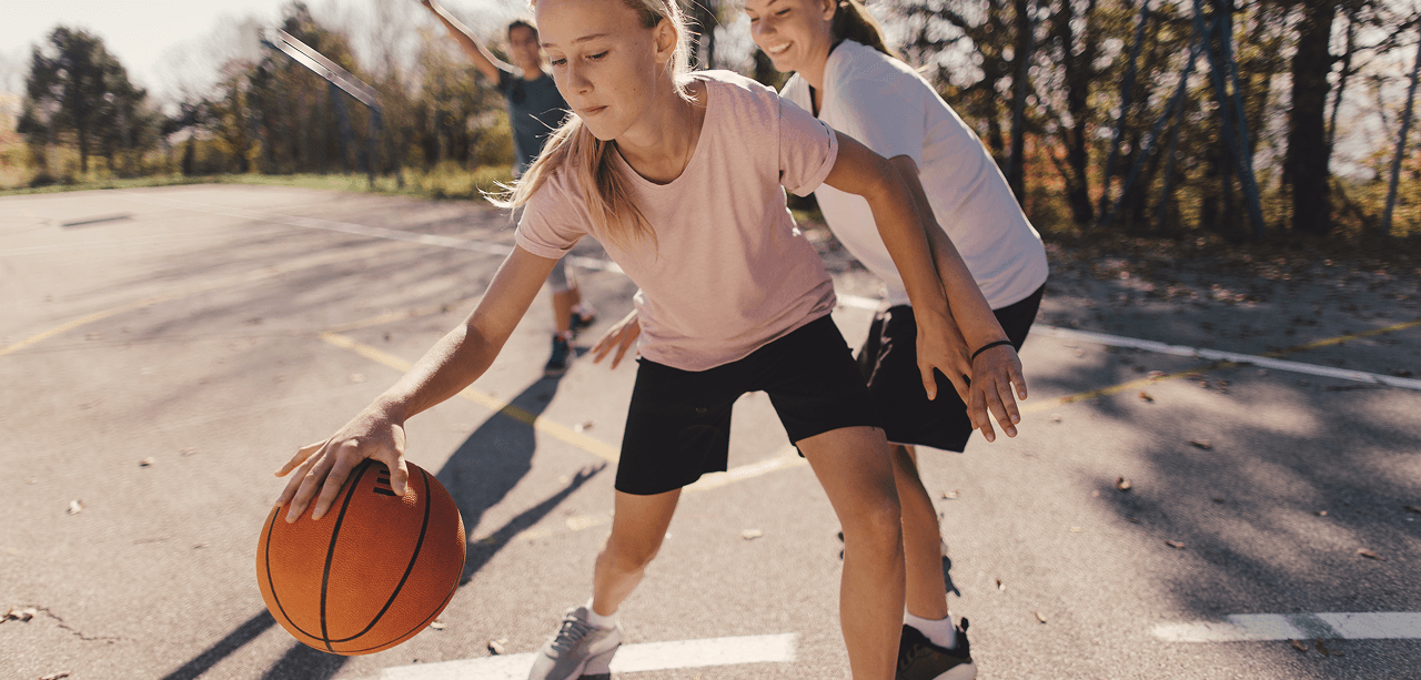 Basketglädje för alla – Låna en boll och spela Barn spelar basket med hjälp av Piffl och en tjej studsar basketbollen.